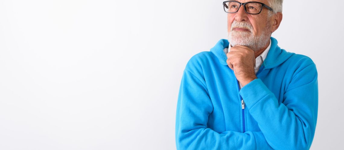 Studio shot of handsome senior bearded man thinking while looking up ready for gym against white background